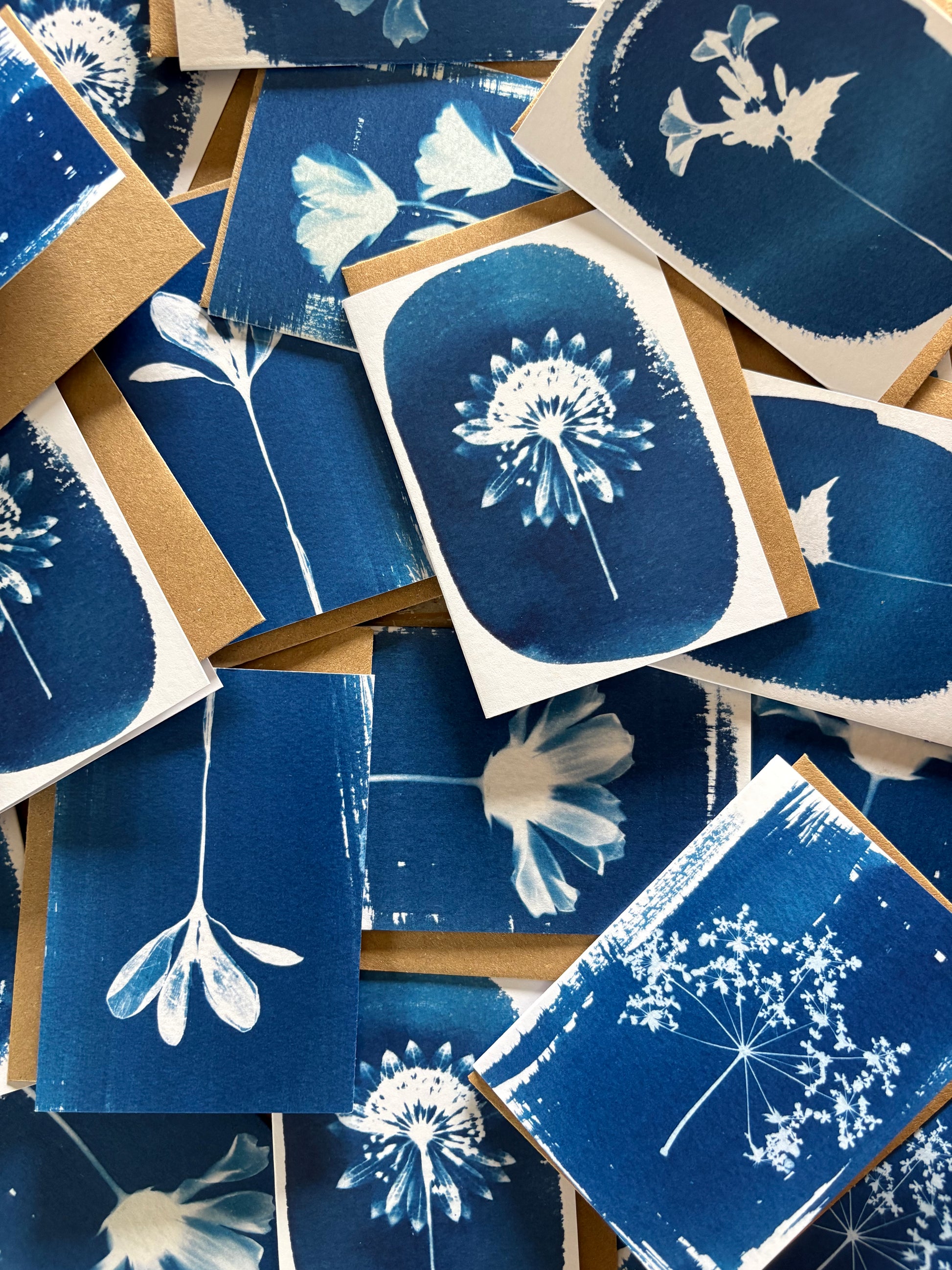 A pile of blue-and-white floral print cards and envelopes with kraft brown backing, arranged overlapping on a light neutral surface.