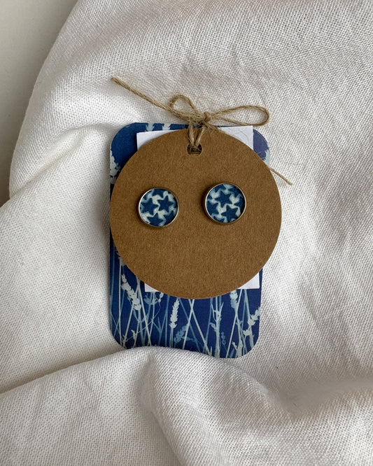 Pair of blue and white patterned earrings on a brown card with a blue and white patterned backing, all on a white fabric background.