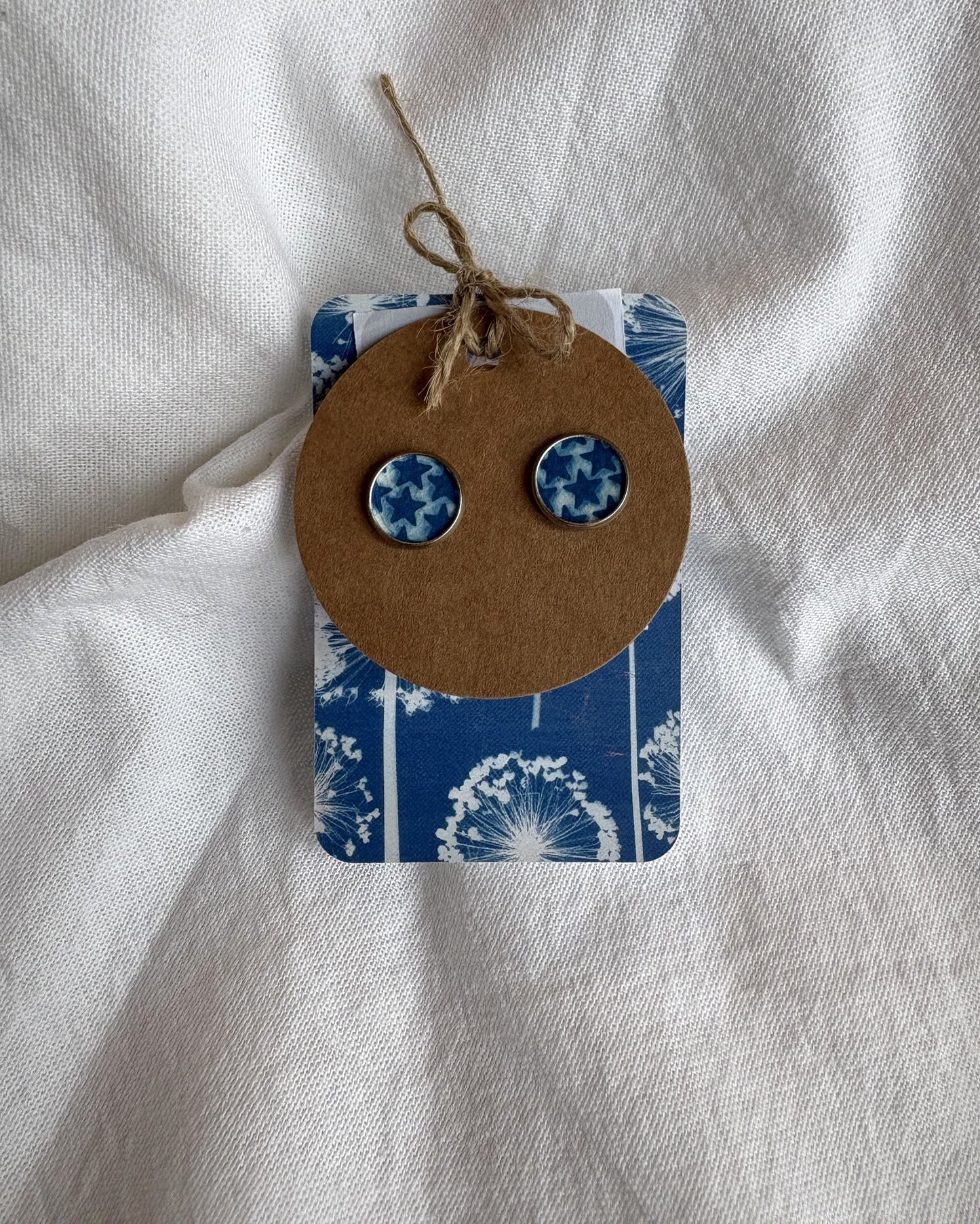 Pair of blue patterned earrings on a brown card with a blue floral design, against a white fabric background.